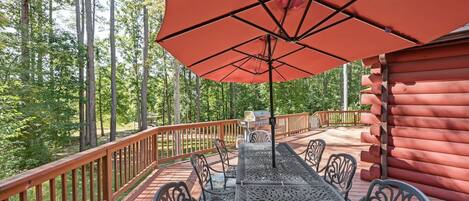A deck with a table and chairs, a red umbrella, and a wooden cabin in a forest.