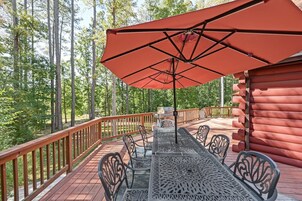 Una terraza con una mesa y sillas, un paraguas rojo y una cabaña de madera en un bosque.