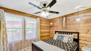 Een slaapkamer met een bed, houten wanden, een plafondventilator en een raam met gordijnen.