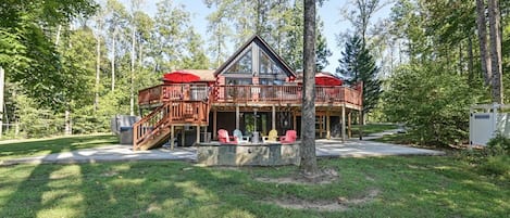 A cabin with a deck, outdoor seating, and a stone fireplace.