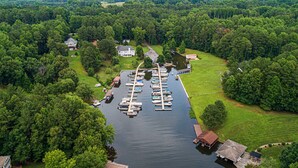Een luchtbeeld van een jachthaven met aangemeerde boten, omgeven door weelderige begroeiing en woonhuizen.