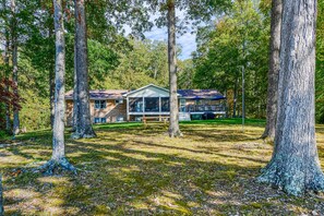 A two-story building with a covered porch, surrounded by trees in a wooded area. - Lakefront Home With Private Dock, Hot Tub, Fireplace, & Central A/C - Free Wifi (Bumpass)