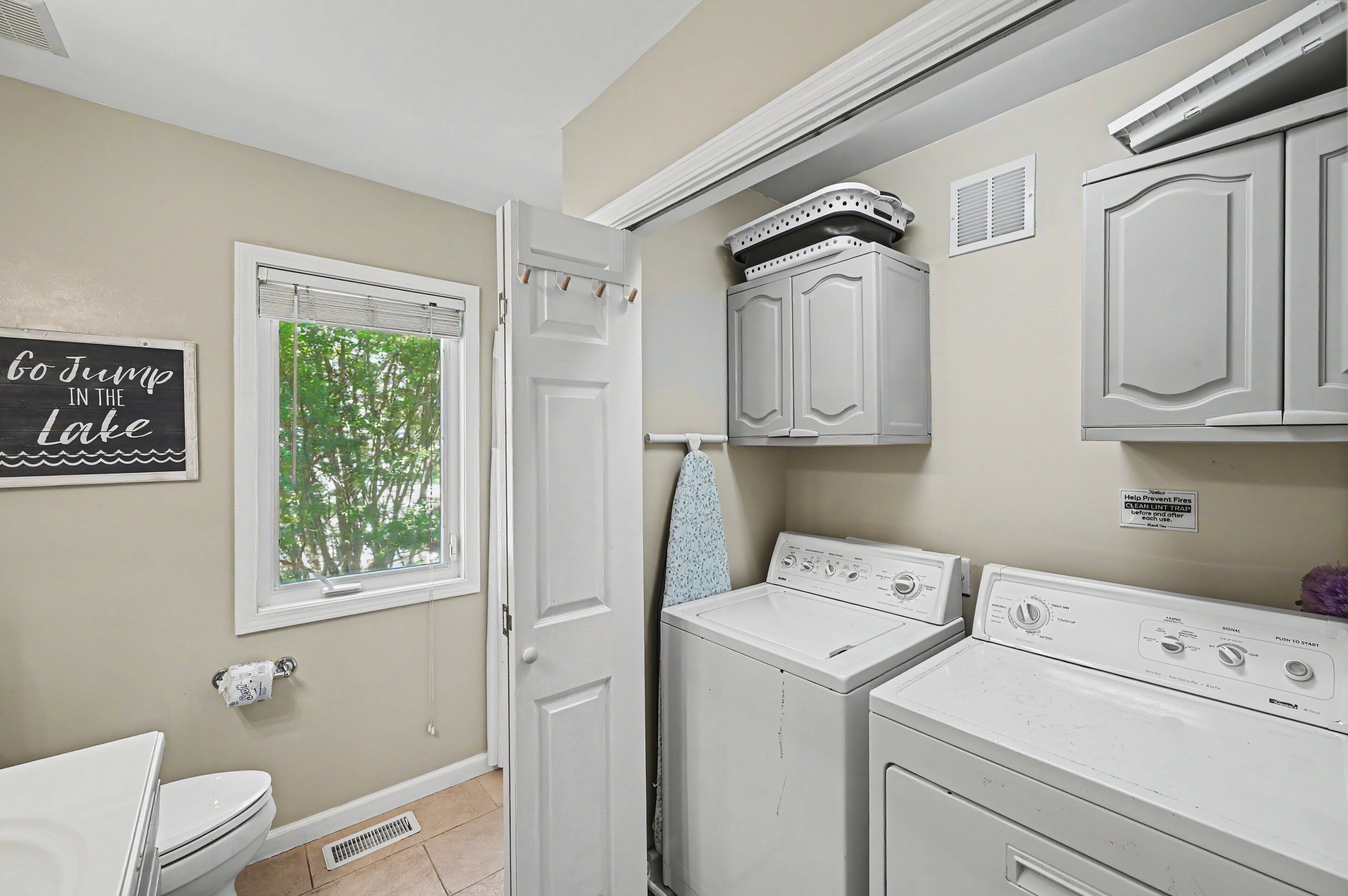 A laundry room with a washer and dryer, a window with a view of trees, and a sign on the wall.
