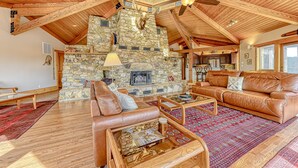 A spacious living area with a stone fireplace, leather sofas, and a high ceiling with exposed beams. - Huge Lakefront Home With A/c, Sunroom, Boat Ramp, Wifi,game Room, Deck, & Kayaks (Louisa)