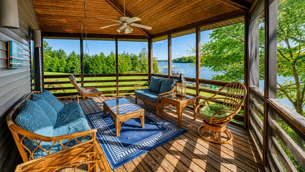 A covered deck with wicker furniture, a ceiling fan, and a view of a lake. - Huge Lakefront Home With A/c, Sunroom, Boat Ramp, Wifi,game Room, Deck, & Kayaks (Louisa)