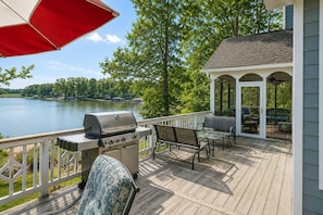Eine Terrasse mit Grill, Gartenmöbeln und einem Pavillon mit Blick auf einen See.