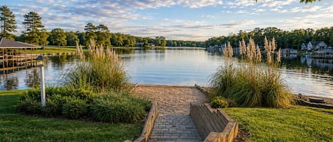 Un camino que lleva a un lago con un quiosco y casas al fondo.