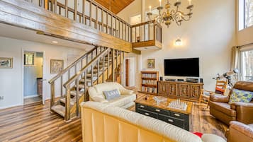 Un salon spacieux avec un grand canapé, une table basse en bois, un téléviseur et un escalier menant à un niveau supérieur.