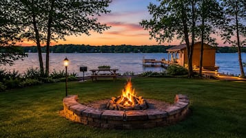 A lakeside deck with a fire pit, picnic table, and a wooden structure.