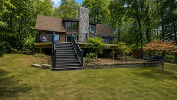 A two-story house with a stone fireplace, a staircase, and a well-maintained lawn.