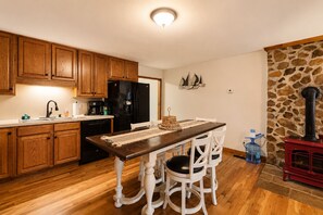 A kitchen with wooden cabinets, a black refrigerator, a dining table with white chairs, and a stone fireplace. - Lake Anna Home on Large Corner lot With Kayaks, Paddleboard, Firepit & Grill (Bumpass)