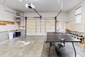 A ping pong table in a room with a garage door, chairs, and a trash can. - Lake Anna Home on Large Corner lot With Kayaks, Paddleboard, Firepit & Grill (Bumpass)