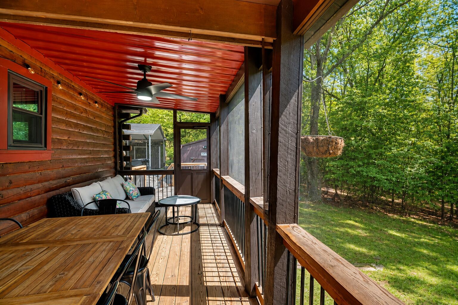 Una terraza de madera con una mesa y sillas, una cesta colgante y vistas a un paisaje verde.