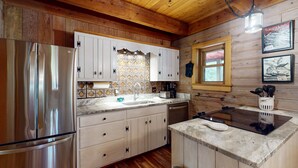 A kitchen with wooden walls, a stainless steel refrigerator, white cabinets, a sink, and a window with a view. - Lakefront House W/waterslide, hot Tub, Game Room, & Wood Fireplace (Mineral)