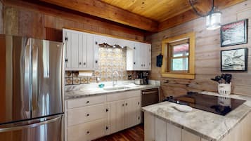 A kitchen with wooden walls, a stainless steel refrigerator, white cabinets, a sink, and a window with a view.
