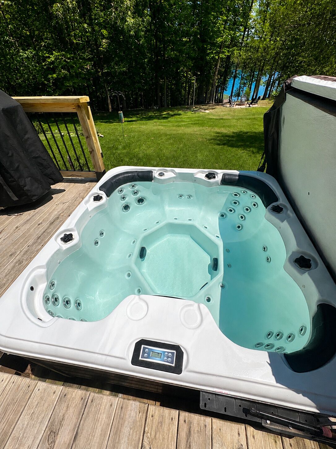 A hot tub on a wooden deck with a grassy yard and trees in the background.