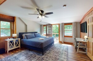 Un dormitorio con cama, escritorio, silla, ventilador de techo y ventanas amplias.