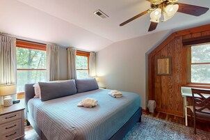 Un dormitorio con cama, escritorio, silla, ventilador de techo y ventana con cortinas.