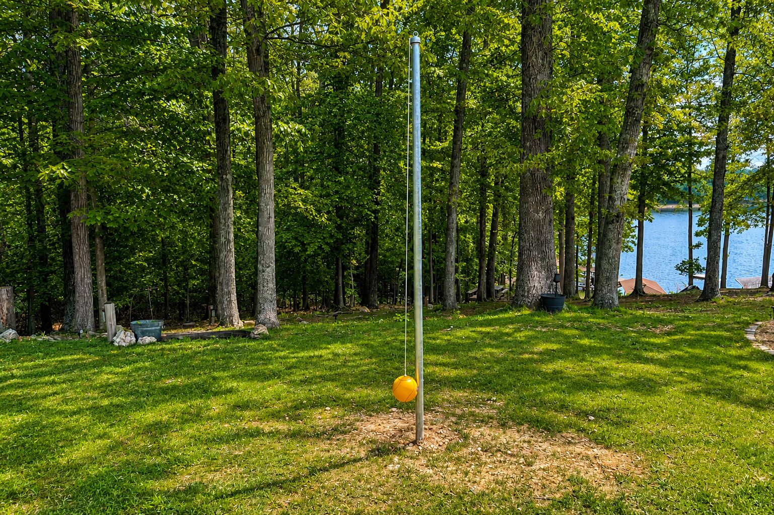 A grassy area with a metal pole and a yellow object, surrounded by trees and a body of water.