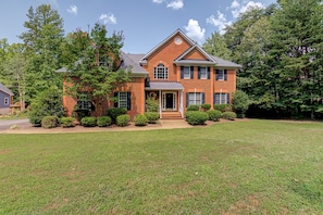 A two-story brick house with a front porch, a garage, and a well-maintained lawn. - Lakefront Home With Boat Dock, Private Firepit & Game Room - Dog-friendly (Bumpass)