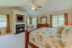 A bedroom with a fireplace, a bed with floral bedding, a ceiling fan, and a large mirror. - Lakefront Home With Boat Dock, Private Firepit & Game Room - Dog-friendly (Bumpass)