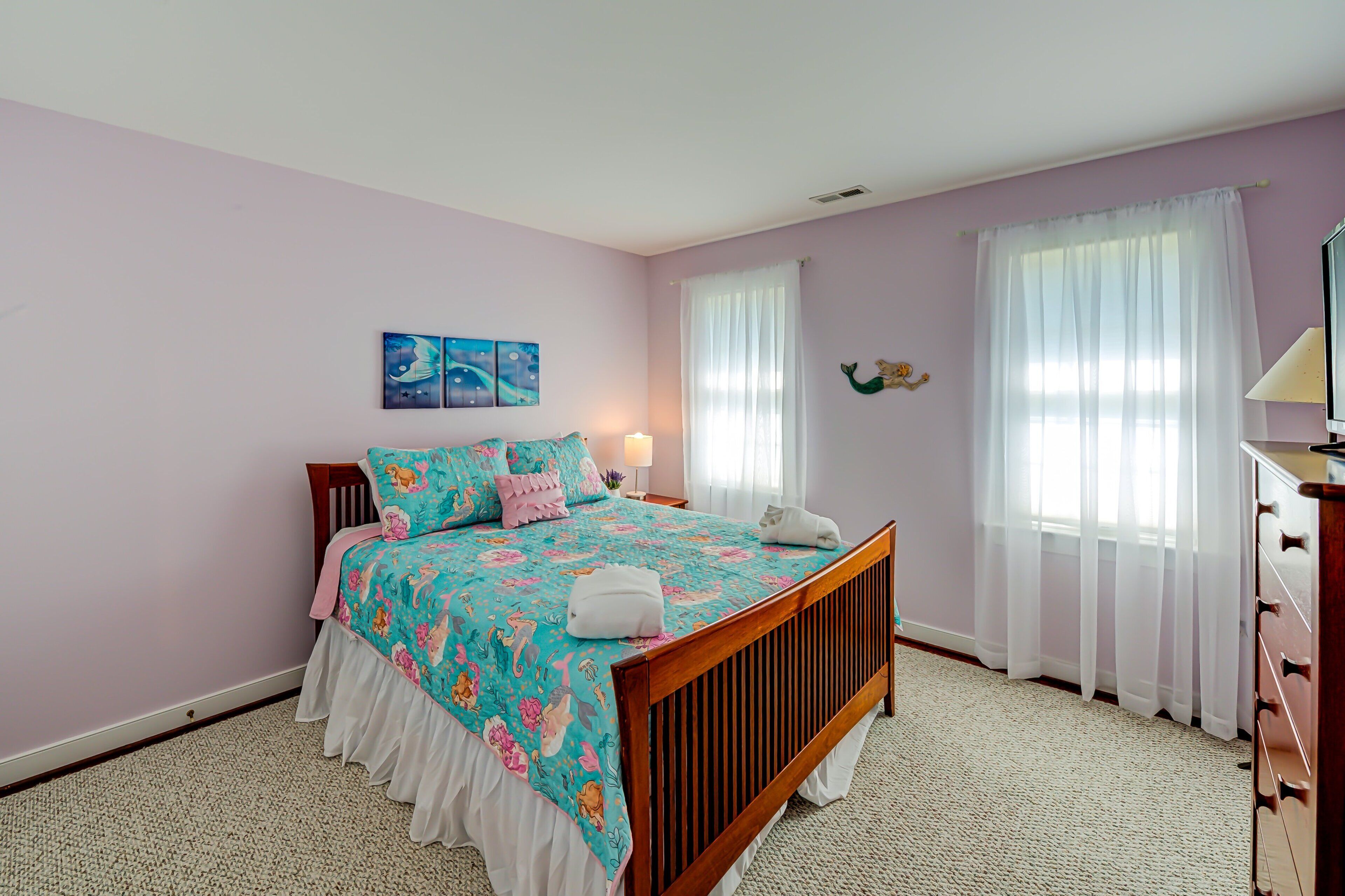 A bedroom with a bed, a dresser, a nightstand, a lamp, and a wall-mounted TV.