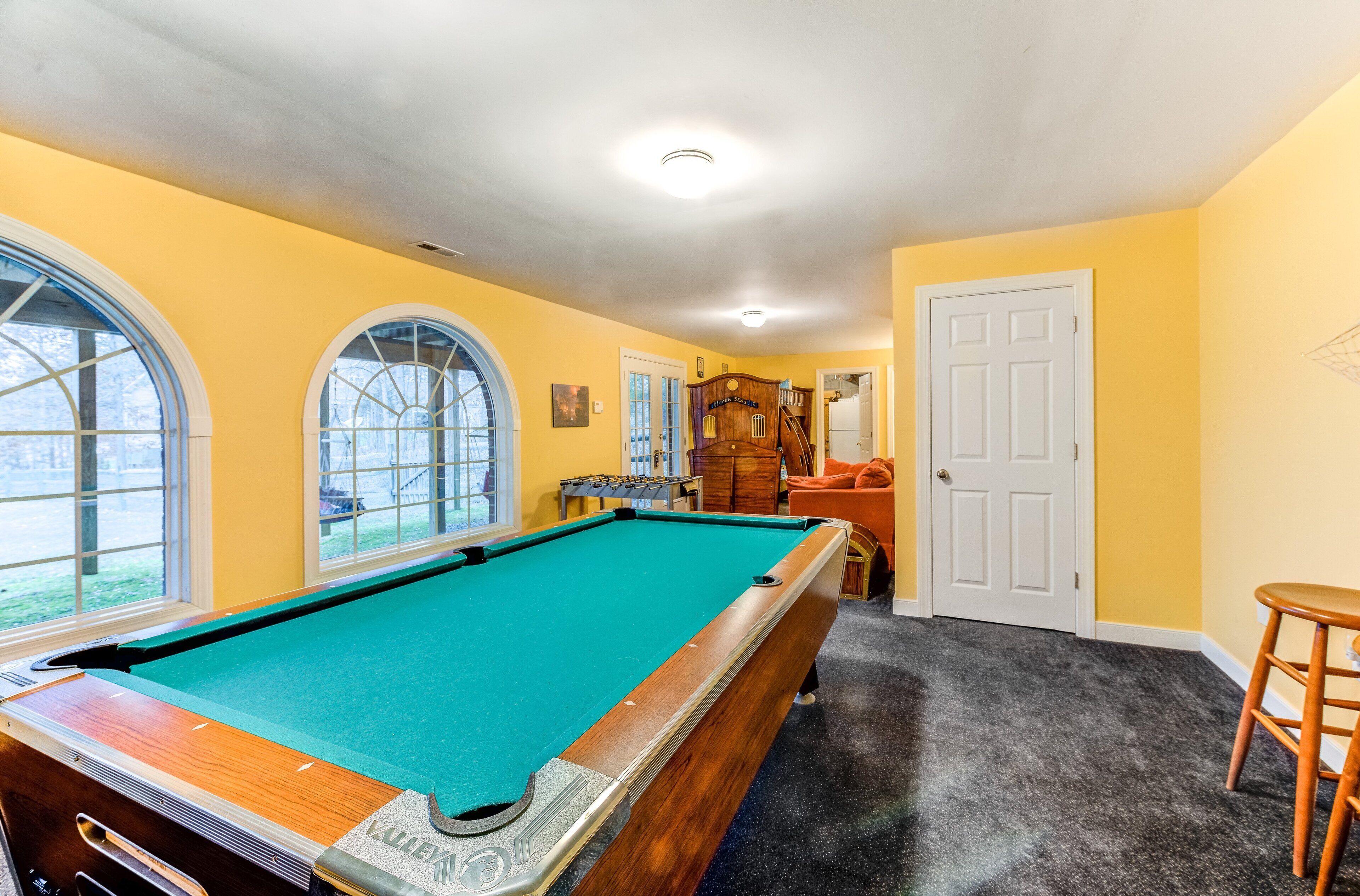 A pool table in a room with yellow walls, a door, and a window.
