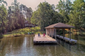 A dock with chairs, a covered area, and a house in a wooded area. - Lakefront Home With Boat Dock, Private Firepit & Game Room - Dog-friendly (Bumpass)