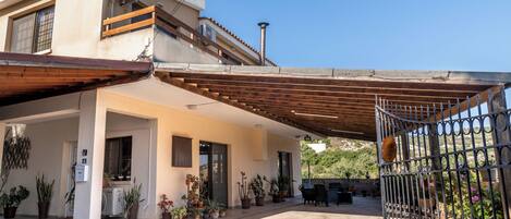 Une maison à deux étages dotée d’un patio couvert, d’un espace salon extérieur et de plantes en pot.