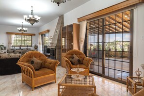 Un salon spacieux, meublĂ© de meubles en osier, avec une table basse en verre et une grande porte-fenĂȘtre coulissante donnant sur un espace extĂ©rieur.