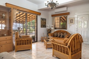 A room with wicker furniture, a chandelier, and large windows.