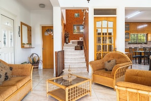 A spacious living area with a staircase, wicker furniture, and a dining area with wooden cabinets.