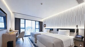 A modern hotel room with two beds, a desk, a chair, a large window with a city view, and a control panel on the nightstand. - Wanda Moments Zhuhai (Zhuhai)