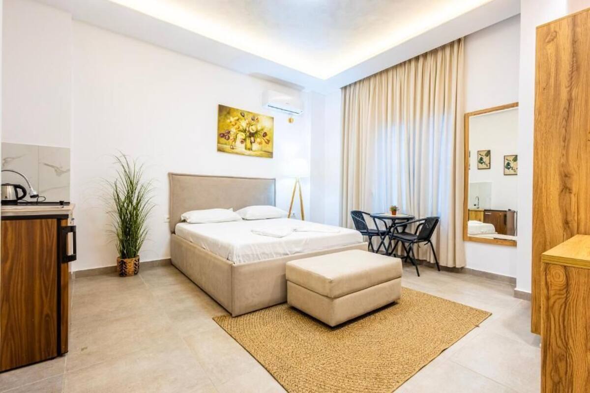Ein modernes Hotelzimmer mit Bett, Schreibtisch, Stuhl, kleinem Tisch, Spiegel und einer Topfpflanze.