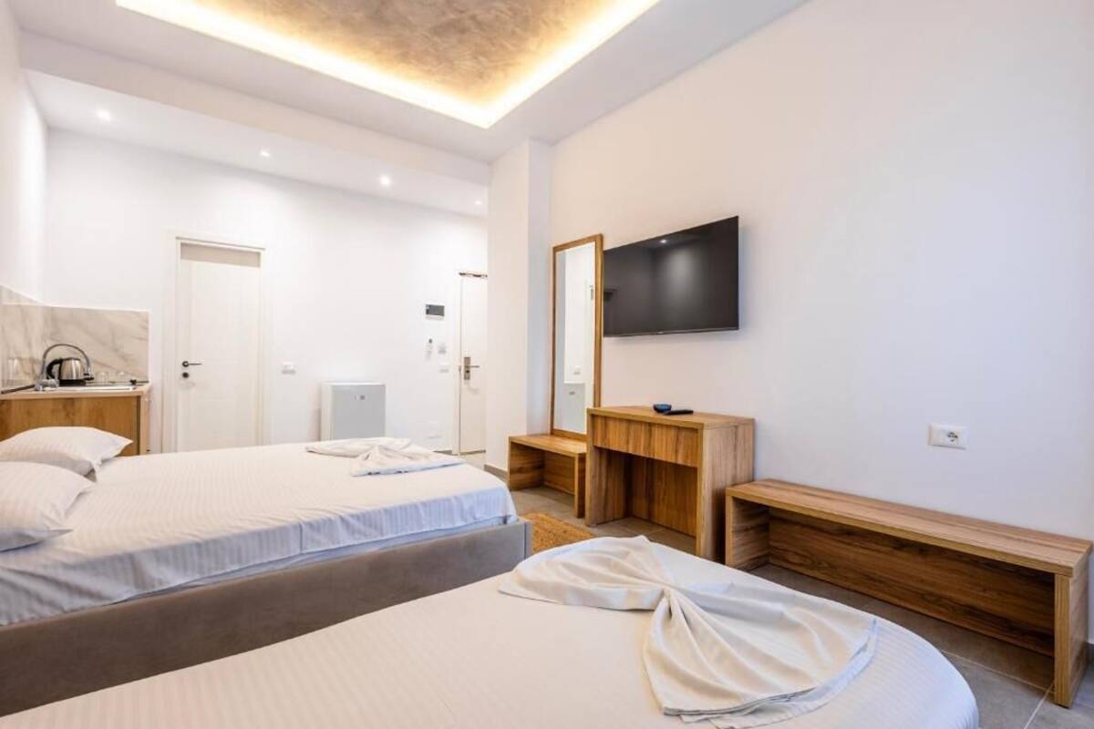 Ein modernes Hotelzimmer mit zwei Betten, einem Fernseher, einer hölzernen Bank und einem Spiegel.
