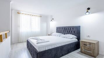 A bedroom with a bed, bedside tables, a nightstand, a window with curtains, and a wall-mounted light fixture.