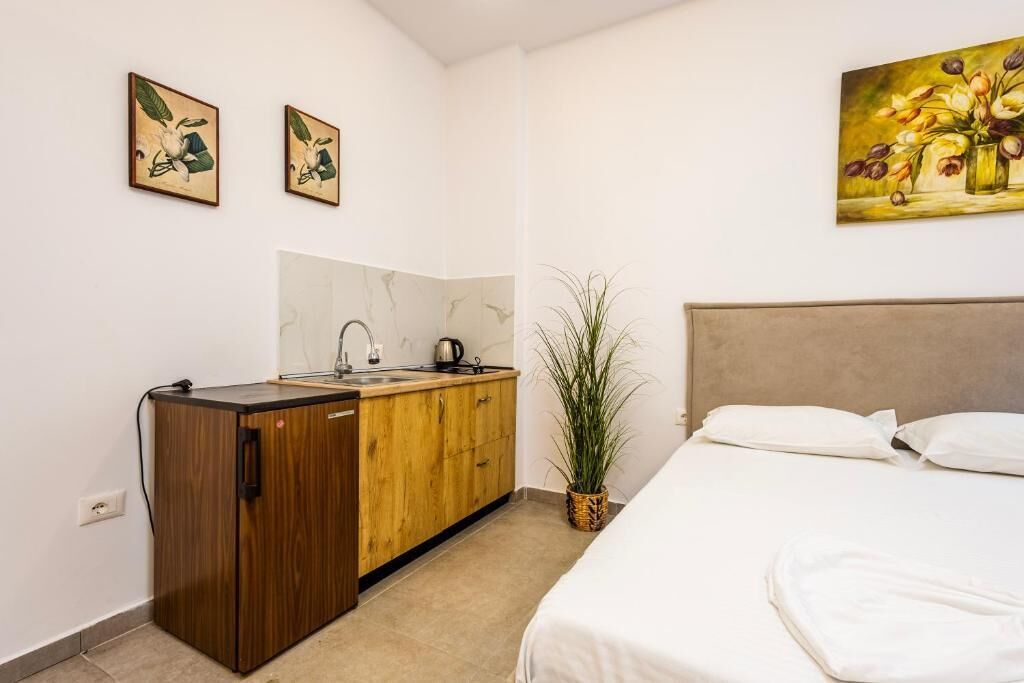 Una camera d'albergo con un letto, un mobiletto in legno, un lavandino e una pianta in vaso.