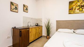 Una camera d'albergo con un letto, un mobiletto in legno, un lavandino e una pianta in vaso.