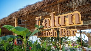 A wooden sign for 'Talun Beach Bar' with a thatched roof and lush greenery.