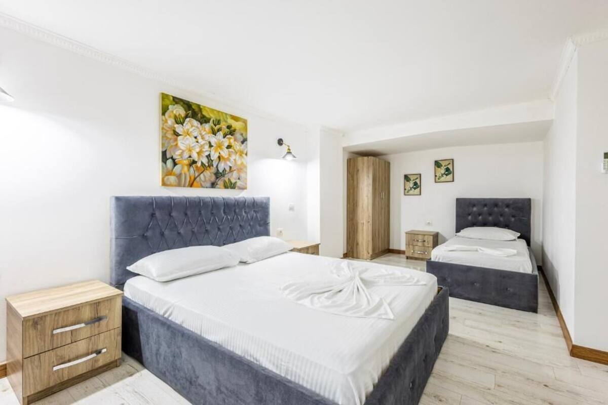 Ein Hotelzimmer mit zwei Betten, einem Holznachtkästchen, einem Gemälde und einer Tür zu einem weiteren Raum.