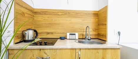Une cuisine dotée de meubles en bois, d’un évier en acier inoxydable, d’une bouilloire et d’un petit plan de travail.