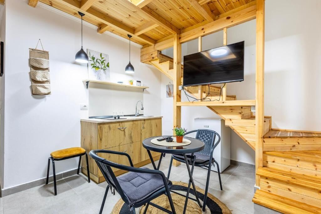 Eine kompakte Küche mit Holzboden, einer an der Wand befestigten Fernseher und einem runden Tisch mit Stühlen.