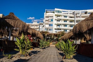 A pathway flanked by thatched-roof structures leading to a modern multi-story building. - LaLun Apartments & Rooms (Golem)