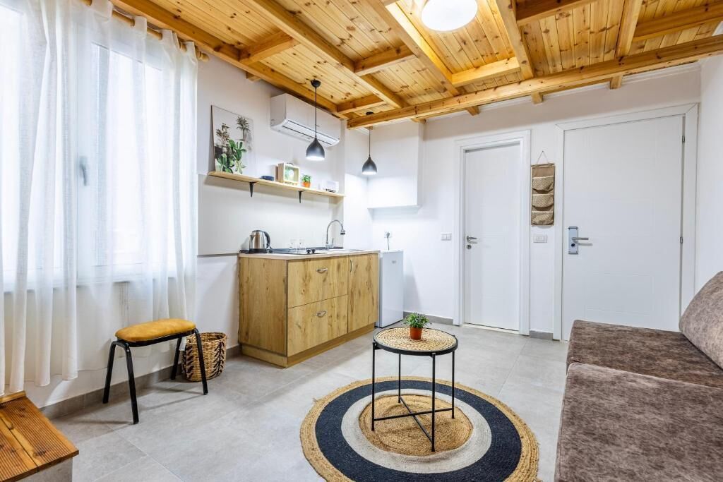 Un espacio habitable pequeño con kitchenette, techo de madera, sofá y una mesa redonda pequeña.