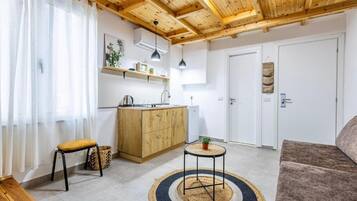 Un espacio habitable pequeño con kitchenette, techo de madera, sofá y una mesa redonda pequeña.