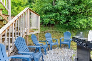 Une terrasse avec des rampes en bois, des chaises Adirondack bleues et un barbecue.