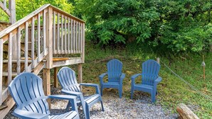 Um deck de madeira com cadeiras Adirondack e uma estrutura de madeira numa área arborizada.