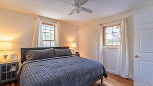 Quarto com uma cama, duas mesas de cabeceira com abajures, um ventilador de teto e uma porta.