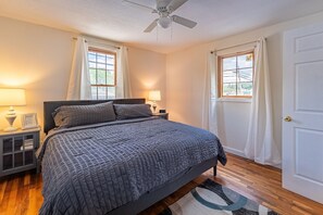 Une chambre à coucher avec un lit, deux tables de chevet avec des lampes, un ventilateur de plafond et une porte.