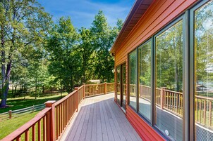 Una terraza de madera con barandillas de vidrio, rodeada de árboles.